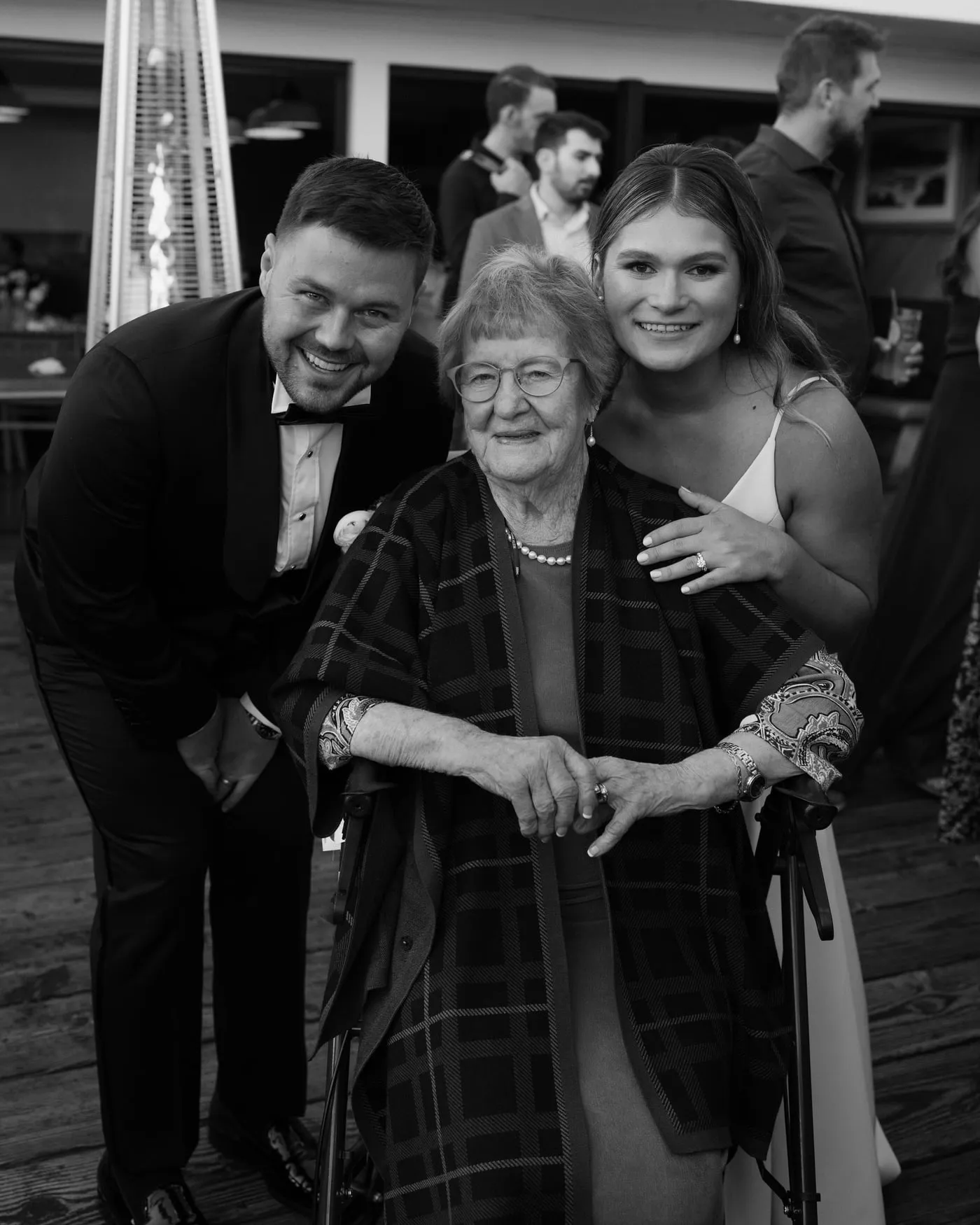 Three of us at an outdoor wedding reception: my grandmother seated in the middle in glasses and a patterned shawl, my wife and me leaning in on either side, all smiling.